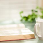 Open book and cup of coffee grace a glass top table.